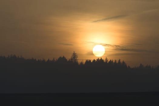Telephoto sunset over a distant coniferous forest at redmires reservoirs near sheffield. Hazy sky as the sun just touches the tree tops. Copy space
