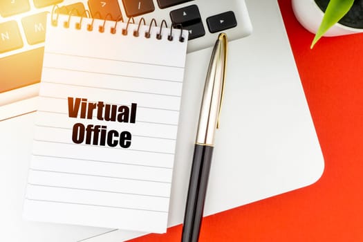 VIRTUAL OFFICE text with notepad, laptop, fountain pen and decorative plant on red background. Business and Copy Space Concept