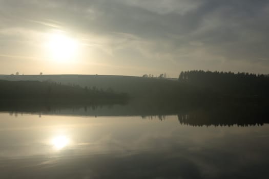 Warm dusky sunset reflected in finely rippled reservoir water at redmires reservoirs near sheffield. Stunning reflected landscape image. Wispy clouds