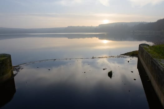 Sunset over redmires reservoirs, taken looking through an inlet to the reservoir dam. Atmospheric image due to the misty haze in front of the forest.