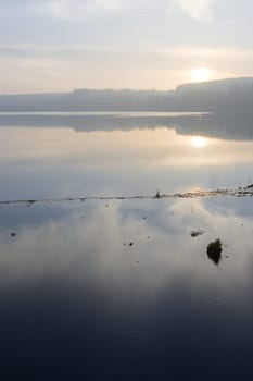 Misty landscape and wispy clouds reflected in calm reservoir water. Vertical sunset image over redmires reservoir, at the top reservoir.