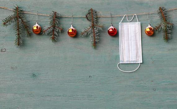 Corona and Christmas. A protective mask hangs next to Christmas tree balls and fir branches