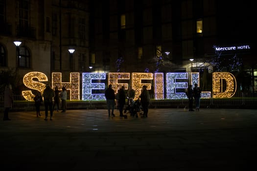 Sheffield, United Kingdom, 27th November, 2020: Close up of Sheffield illuminated with christmas fairy lights. groups of people stand in front.