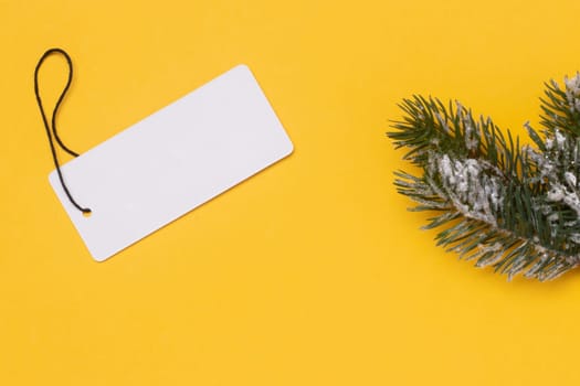 Template for christmas sale. A blank paper price tag and a fir branch on a yellow background. Concept of winter or Black Friday sale. Empty space for design.