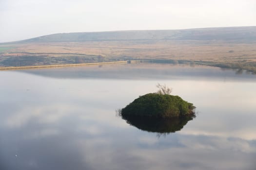 Reflected sky in calm reservoir water, moors in the sunny background. Reservoir wall runs along the left hand side, taken at redmires near sheffield