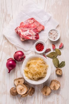 Ingredients for hearty sour cabbage soup (sauerkraut soup) with meat, onioc, garlic and spicies on wooden table