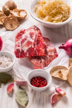 Ingredients for hearty sour cabbage soup (sauerkraut soup) with meat, onioc, garlic and spicies on wooden table