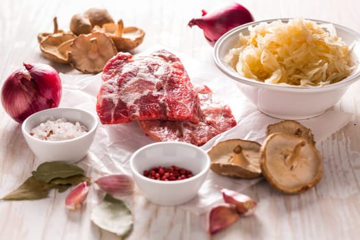 Ingredients for hearty sour cabbage soup (sauerkraut soup) with meat, onioc, garlic and spicies on wooden table