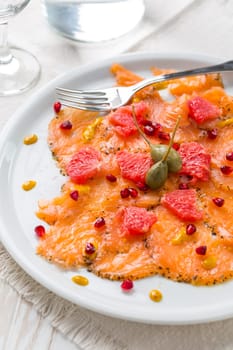 Salmon carpaccio with pink grapefruit and pomegranate on white plate