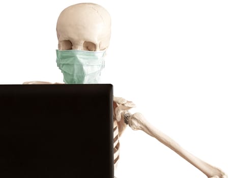 The skeleton in protective medical mask works with the laptop