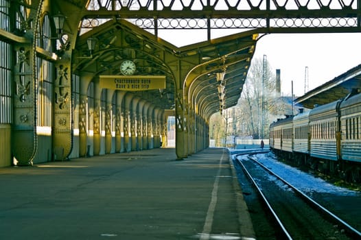 Railroad station platform with a hanging clock and "Have a nice trip"" signboard."