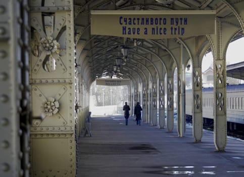 Railroad station platform with a hanging clock and "Have a nice trip"" signboard"