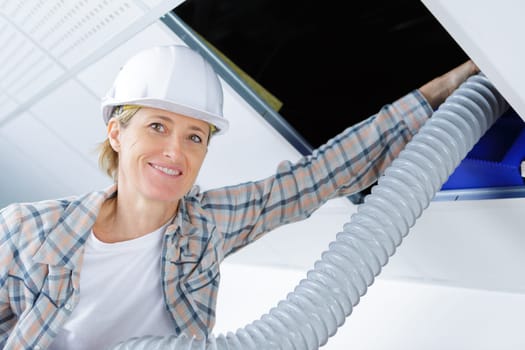female worker fitting ventilation system in buildings ceiling