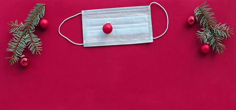 Corona and Christmas. A protective mask next to Christmas tree balls and fir branches on a pink background