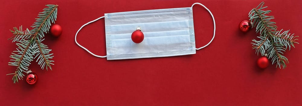 Corona and Christmas. A protective mask next to Christmas tree balls and fir branches on a red background