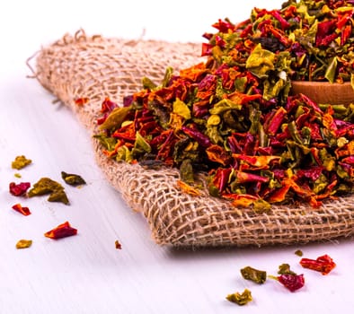 The colored spices with pepper in a cup and burlap on a wooden table