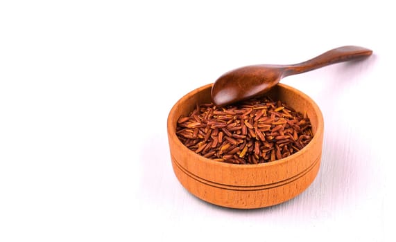Brown rice and spoon in a wooden cup on a white dining table
