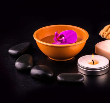 The beautiful spa composition with pink orchid on cup, stones and white gloves on black wooden table