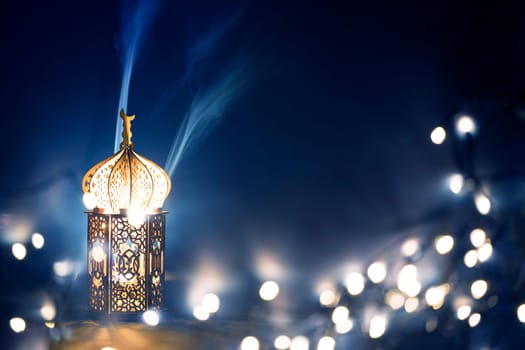 Ornamental Arabic lantern with burning candle glowing at night and glittering golden bokeh lights. Festive greeting card for Muslim holy month Ramadan Kareem.