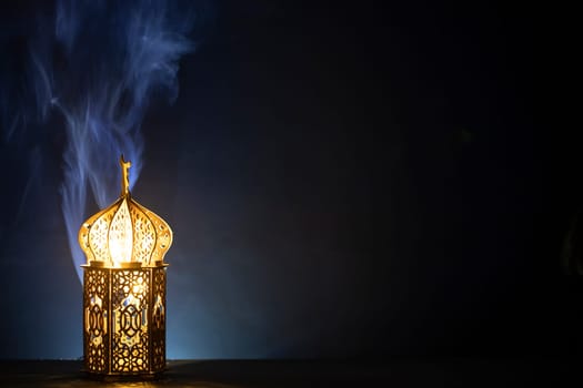Ornamental Arabic lantern with burning candle glowing at night and glittering golden bokeh lights. Festive greeting card for Muslim holy month Ramadan Kareem.