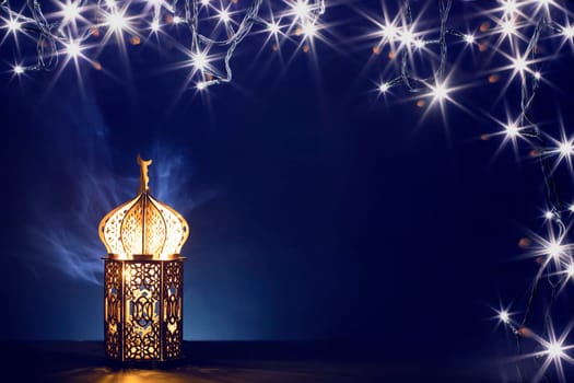 Ornamental Arabic lantern with burning candle glowing at night and glittering golden bokeh lights. Festive greeting card for Muslim holy month Ramadan Kareem.