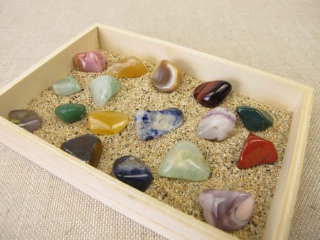 Tumbled gemstones in a wooden box with sand