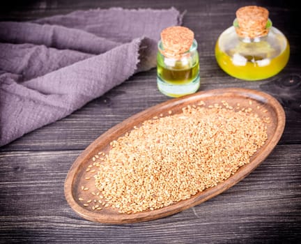 Sesame oil in glass and seeds on lod wooden background