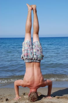 A sporty,muscular young man does a handstand on the beach.