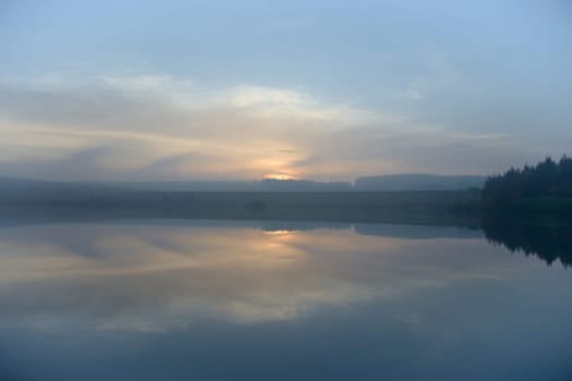 Sunset reflected over calm water. The abstract reflection of the sky forms a symmetrical background image. Wide angle image with a forest to the right