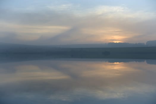 Pastel colors and wispy clouds hang in the sky just after the sun has set over redmires reservoirs. In the peak district near to sheffield.