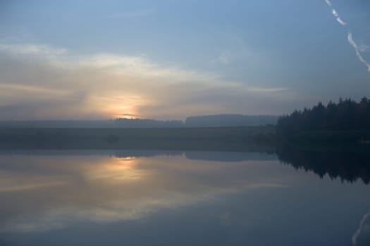 Low clouds mask a misty sunset on the horizon. Taken at dusk over redmires reservoirs, the still water mirrors the sky and cloud scape.