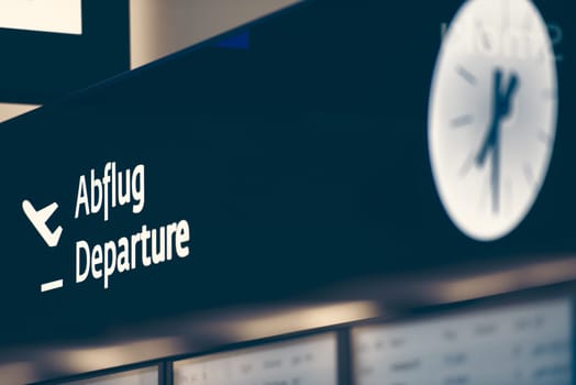 Close up view of black sign with big white inscription Departure and clock. Arit trips and travelling.