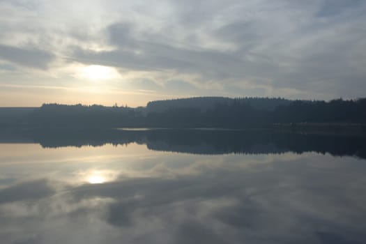 Wide angle symmetrical water reflection landscape during winter at redmires reservoirs near sheffield. Striking cloudscape and forest line reflected