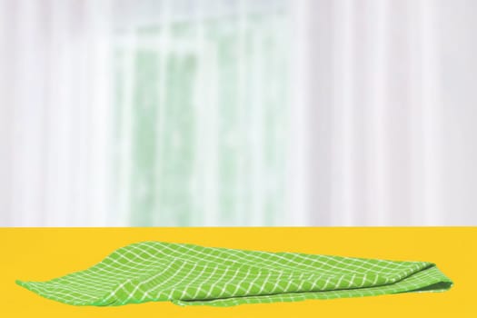 Empty table product. Closeup of a empty green checkered tablecloth or napkin on a yellow table over abstract blurred curtain background. Template for your food and product display montage.