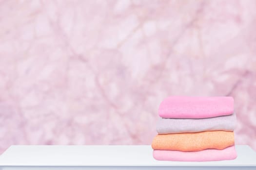 A pile of colorful cozy warm sweaters on a bright table against abstract blurred pink background. Autumn and spring clothes. Space for product display montage.