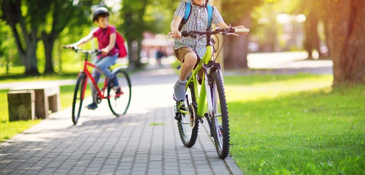 Children with rucksacks riding on bikes in the park near school. Pupils with backpacks outdoors