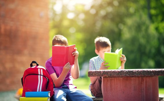 Children with rucksacks sitting in the park near school. Pupils with books and backpacks outdoors