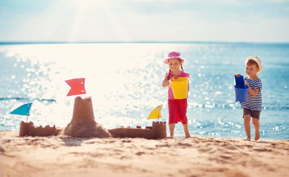 Boy and girl playing on the beach on summer holidays. Children building a sandcastle at sea