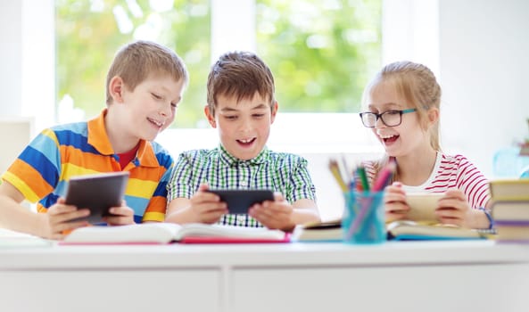 Children sitting in the room with smart phones. Pupils surfing at school