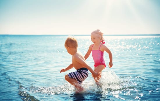 Boy and girl playing on the beach on summer holidays. Children in nature with beautiful sea, sand and blue sky. Happy kids on vacations at seaside running in the water
