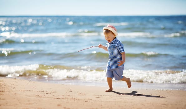 Boy walking at sea in straw hat. Child on vacation in summer at the beach