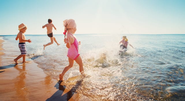 Boys and girls playing on the beach on summer holidays. Children in nature with beautiful sea, sand and blue sky. Happy kids on vacations at seaside running in the water