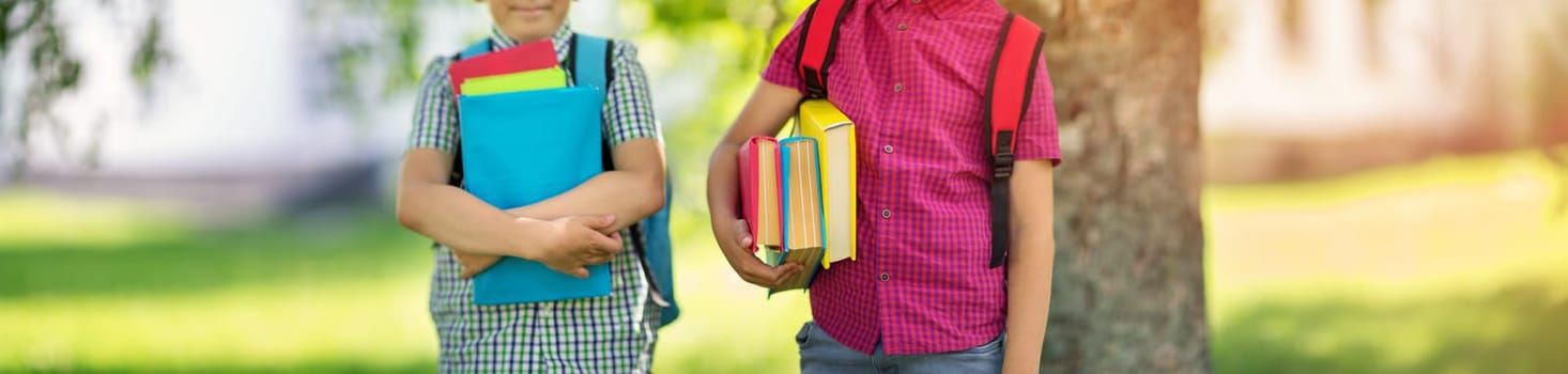 Children with rucksacks standing in the park near school. Pupils with books and backpacks outdoors