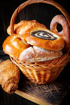 Composition with bread and rolls in wicker basket on dark background, vertical image
