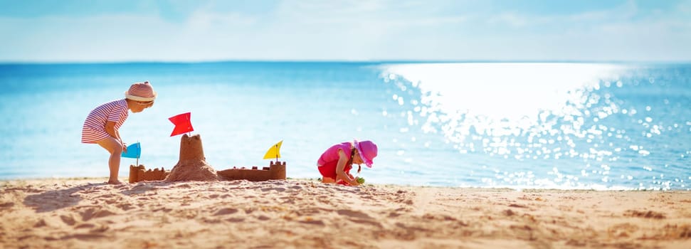 Boy and girl playing on the beach on summer holidays. Children building a sandcastle at sea