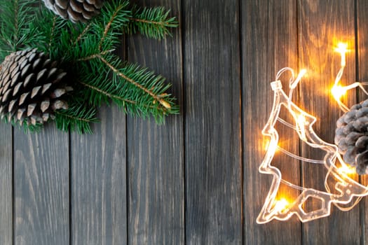 Christmas tree branches, pine cones and garlands on dark wooden background, top view with copy space