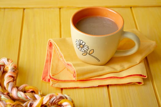 Color concept. Cappuccino with coffee art in orange cup on yellow wooden table.