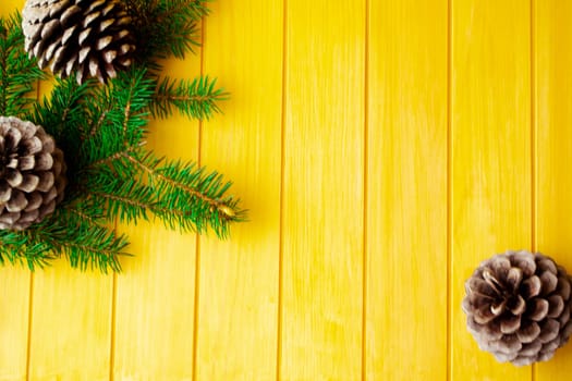 frame made with Christmas pine tree branches and cones on old yellow wooden board. Space for text. Flat lay