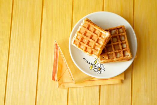 Two delicious waffles on yellow and orange background flat lay