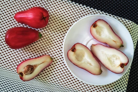 three halves of pomarosa fruit in a plate on a white surface and more fruits aside